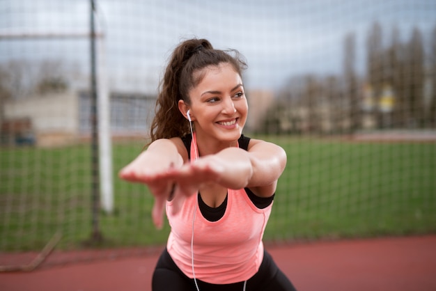 サッカー場近くの彼女の前で手をつないで運動している美しい健康的な笑顔の女の子。