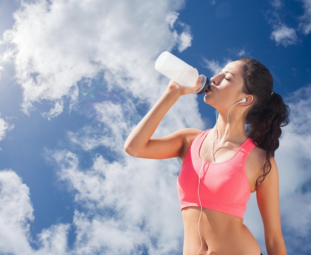 雲と明るい青空に対して水を飲む健康美人