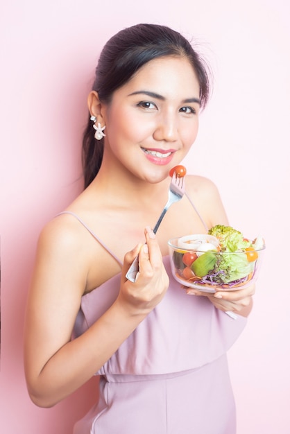 Beautiful Healthy young woman eating salad  on pink  background 