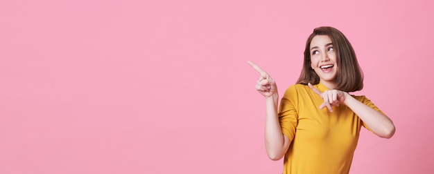 Beautiful healthy young woman smiling with his finger pointing and looking at on light pink with copy space.