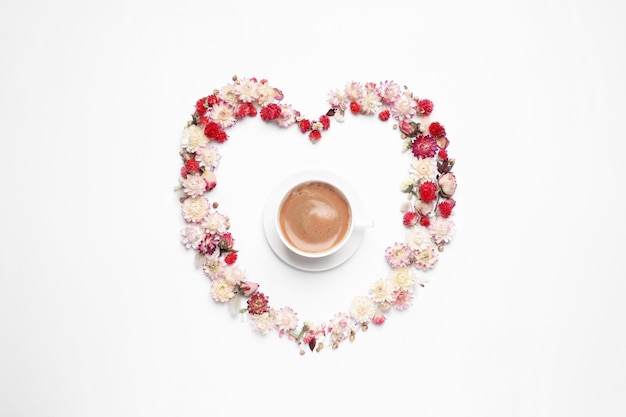Beautiful heart shaped floral composition with cup of coffee on light background flat lay