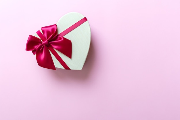 Beautiful heart shaped gift box with red silk bow on a pink background with copy space.