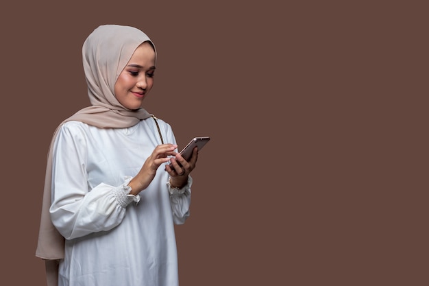 beautiful hijab woman is typing a message on her cell phone with smile expression