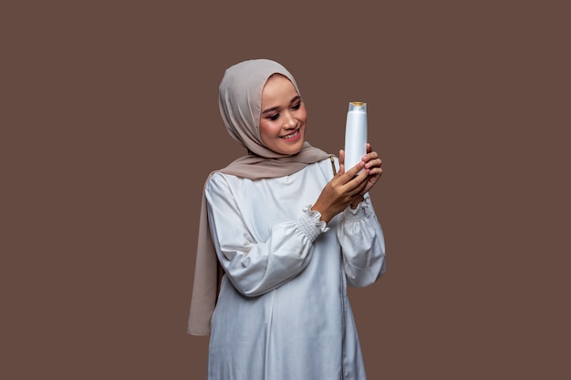 Beautiful hijab woman was holding shampoo bottle in both hands while looking at the bottle.