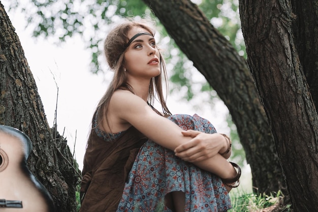 Beautiful hippie girl sitting near big trees in the forest