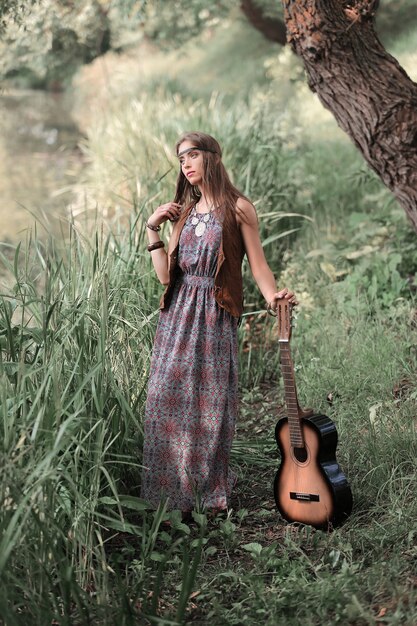 beautiful hippie girl with guitar standing near the pond