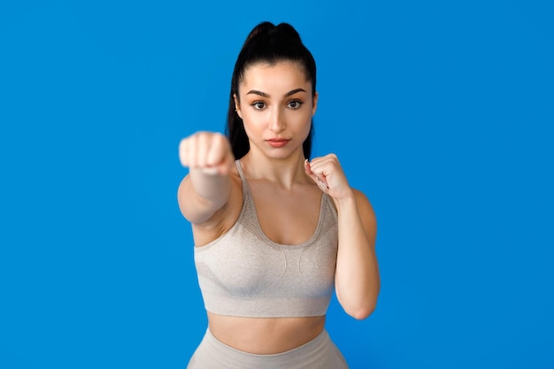 Beautiful hispanic lady punching at camera blue background