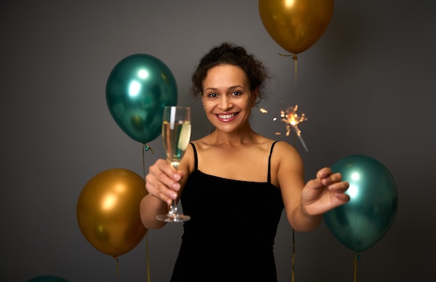 Beautiful Hispanic woman holds a flute of champagne and sparklers smiles with beautiful toothy smile