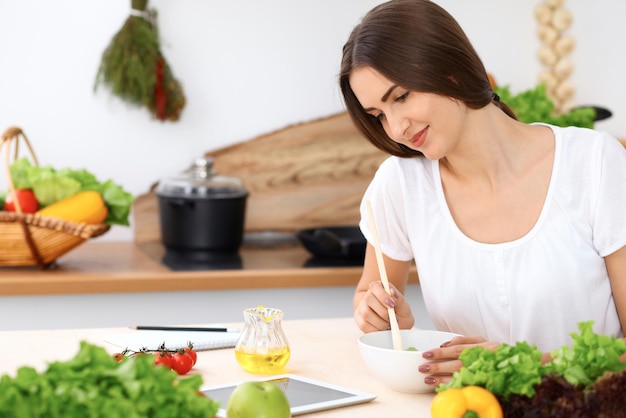 Beautiful  Hispanic woman is cooking in the kitchen. Housewife is tasting fresh salad while sitting at the table