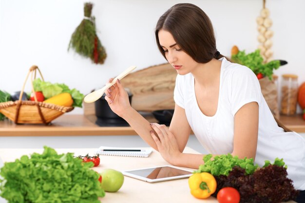 Beautiful Hispanic woman is making online shopping by tablet computer and credit card or searching internet for a new recipe