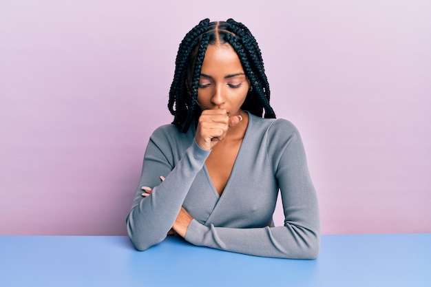 Beautiful hispanic woman wearing casual clothes sitting on the table feeling unwell and coughing as symptom for cold or bronchitis health care concept