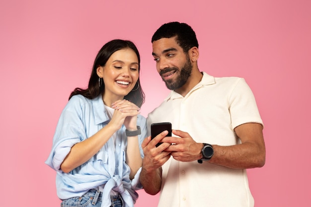 Beautiful hispanic young couple using smartphone on pink background