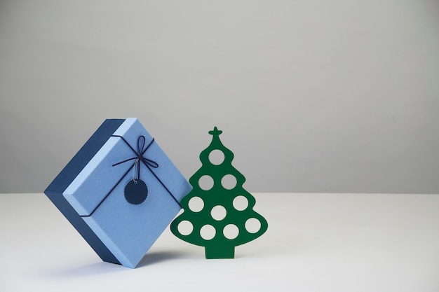 Красивый праздник украшен рождественской елкой с синей бумажной рождественской подарочной коробкой на белом столе