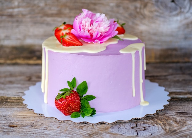 Photo beautiful homemade cake with purple cheese cream, decorated with live pink peony and strawberry berries