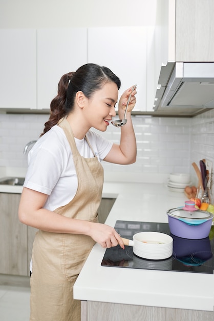 Beautiful housewife cooking with ladle  in kitchen