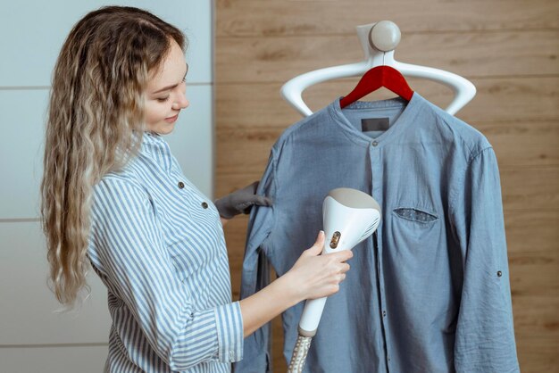 Beautiful housewife irons her shirt inside the house with a steamer Laundry and dry cleaning