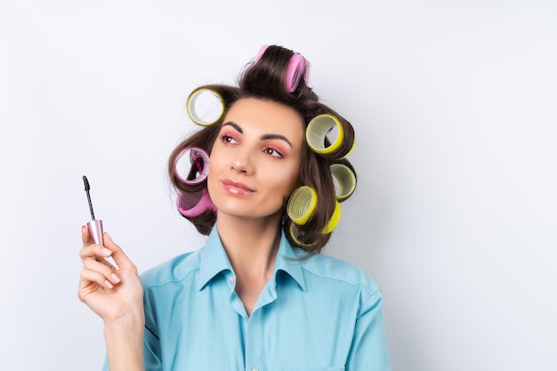 Beautiful housewife A young cheerful woman with hair curlers bright pink makeup and mascara is preparing for a date night dinner on a white background