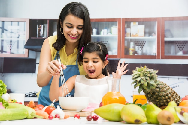 Beautiful Indian or Asian young Mother and Daughter in kitchen, with table full of fruits and vegetables