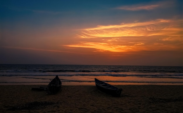 夕方には美しいインドのビーチで、前景に劇的な空とシルエットのボートが見えます