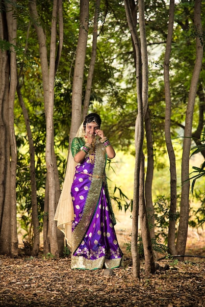 Фото Красивая индийская невеста в традиционном сари позирует на открытом воздухе в парке