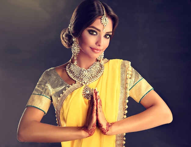 Beautiful indian girl dressed in a traditional national suit mehndi henna tattoo is painted on her hands and traditional kundan style jewelry set is showing a gesture of greeting  namaste