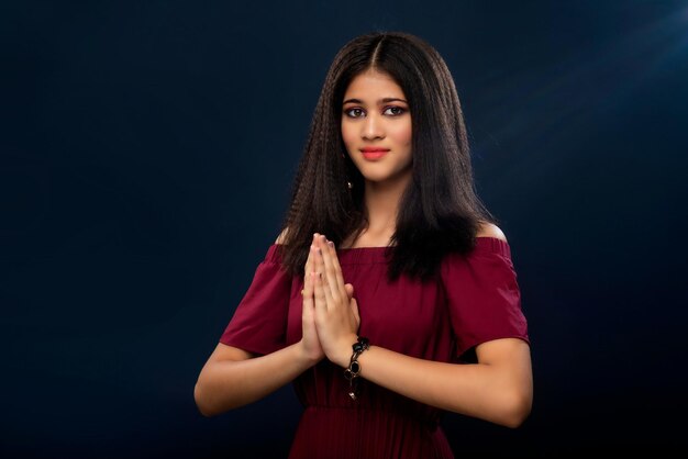 Beautiful Indian girl with welcome expression or inviting or greeting Namaste on a grey background