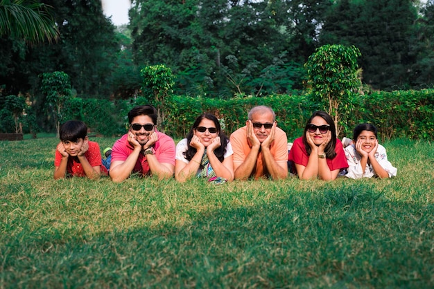 Foto bella famiglia indiana di sei generazioni, che guarda la macchina fotografica e sorride mentre giace insieme sull'erba verde in giardino con le mani sul mento