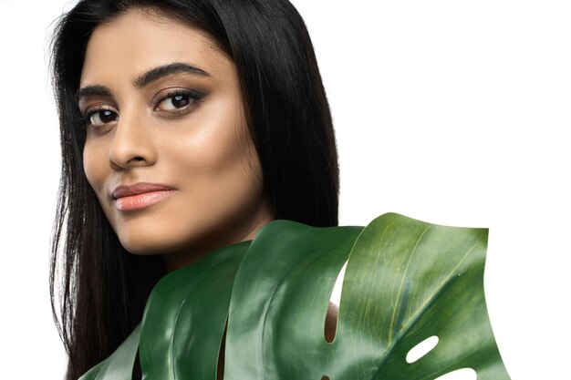 Beautiful Indian woman with a smooth skin holding green tropical leaf on white background