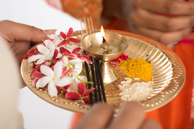 Beautiful Indian young girl holding pooja thali or performing worship on a white wall