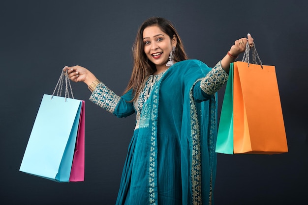 Красивая индийская молодая девушка держит и позирует с хозяйственными сумками на сером фоне