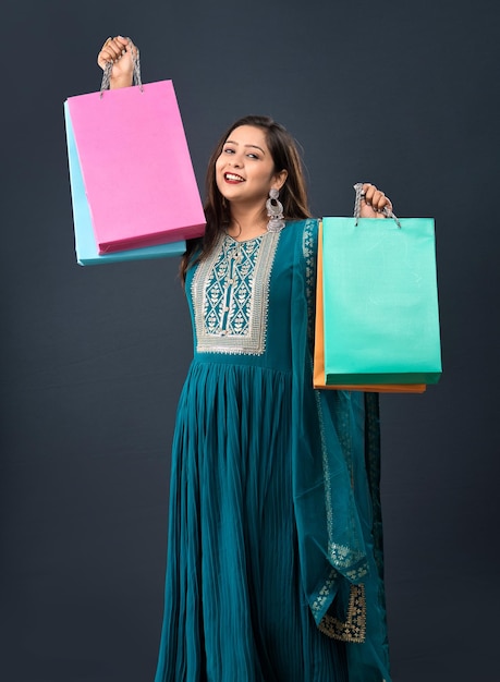 Beautiful Indian young girl holding and posing with shopping bags on a grey background