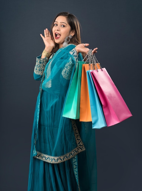 Красивая индийская молодая девушка держит и позирует с хозяйственными сумками на сером фоне