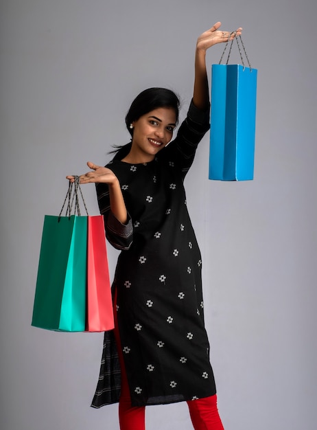 Красивая индийская молодая девушка держит и позирует с сумками на сером