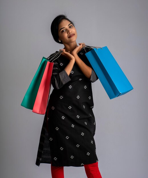 Beautiful Indian young girl holding and posing with shopping bags on grey