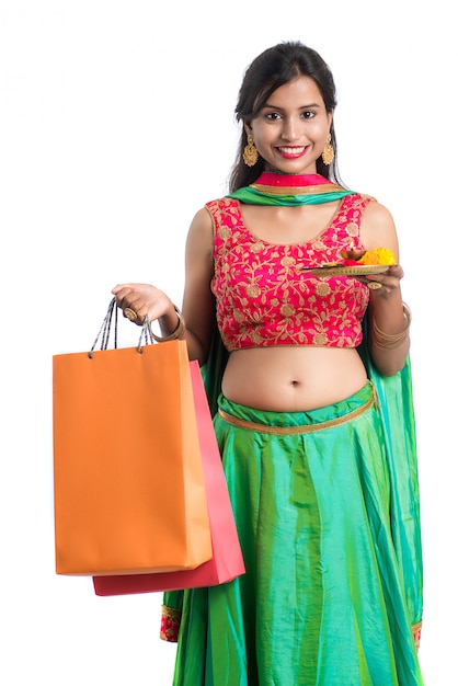 Красивая индийская молодая девушка держит и позирует с хозяйственными сумками и пуджа тхали на белом пространстве