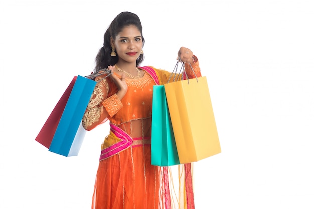 Beautiful Indian young girl holding shopping bags while wearing traditional ethnic wear. Isolated on a white wall