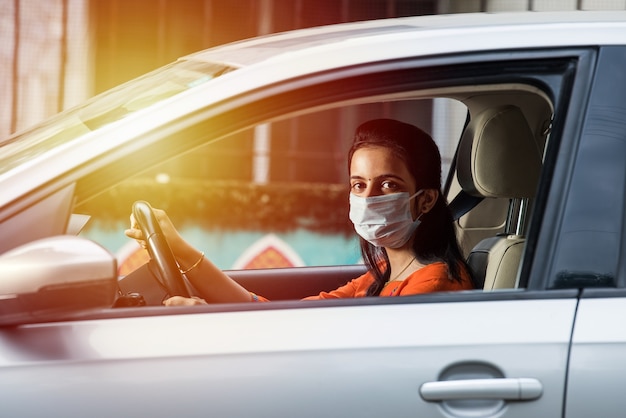 Beautiful Indian young girl in a mask sitting in a car, protective mask against coronavirus, driver on a city street during covid-19 pandemic