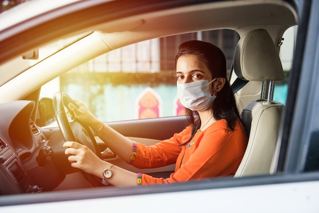 Beautiful Indian young girl in a mask sitting in a car, protective mask against coronavirus, driver on a city street during covid-19 pandemic