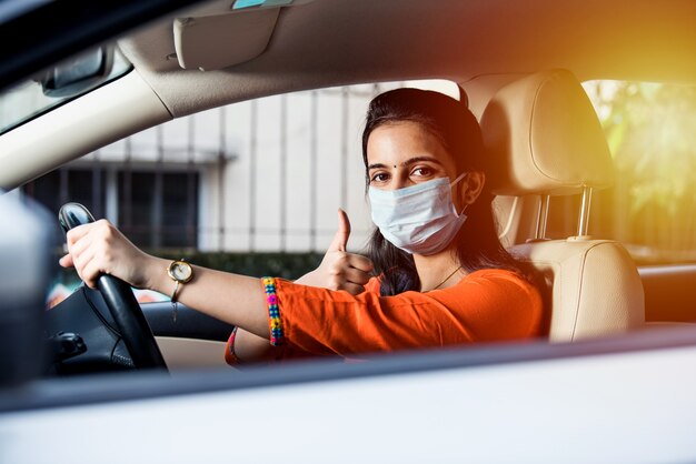 Beautiful Indian young girl in a mask sitting in a car, protective mask against coronavirus, driver on a city street during covid-19 pandemic