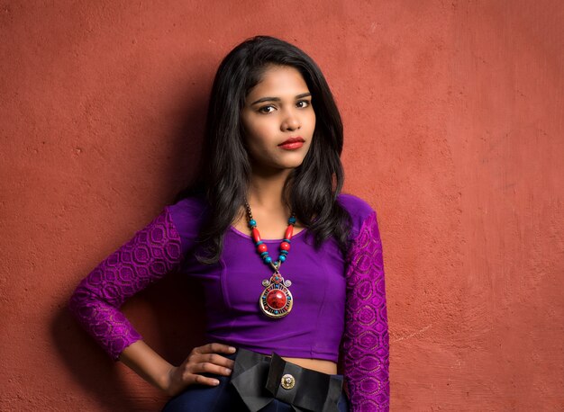 Beautiful Indian young girl posing outdoors on red wall.