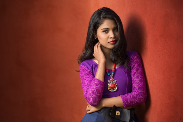 Beautiful Indian young girl posing outdoors on red wall.