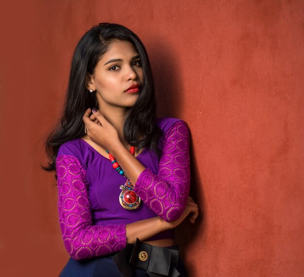 빨간 벽에 야외에서 포즈를 취하는 아름 다운 인도 소녀.