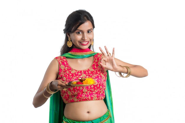 Beautiful indian young woman holding pooja thali or performing worship on a white wall