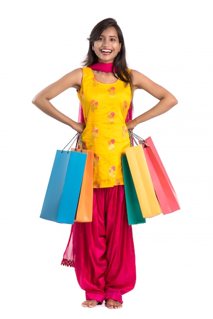 Красивая индийская молодая женщина держа и представляя с хозяйственными сумками на белизне