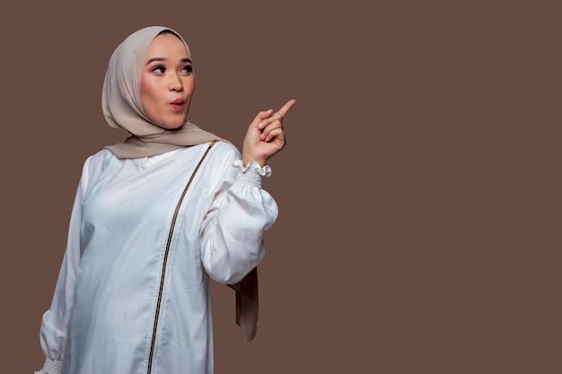 Beautiful indonesian woman wearing hijab is pointing to the right side with surprise expression