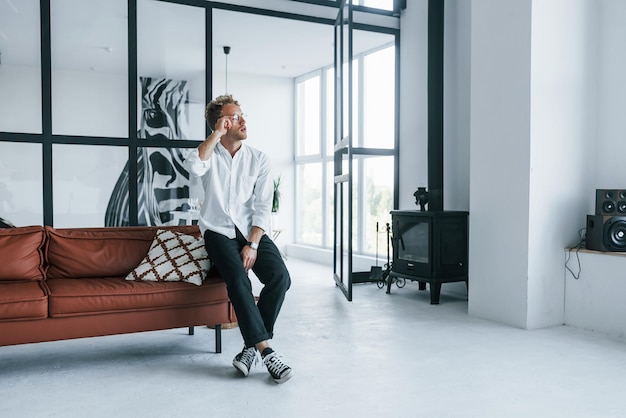 Beautiful interior Caucasian young guy in elegant white shirt indoors at home