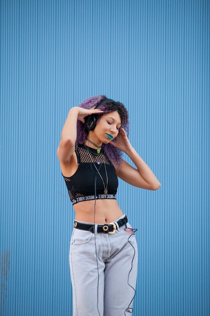 Beautiful interracial teenager listening to music with big headphones on a blue wall