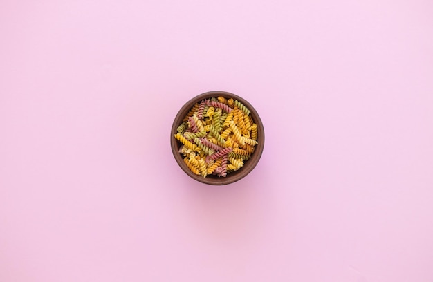 Beautiful Italian uncooked colored farfalle pasta closeup on pink background horizontal top view