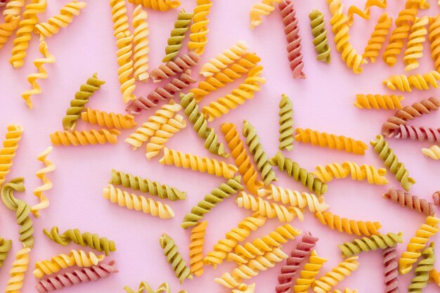 Foto bellissimo primo piano di pasta colorata italiana non cotta su sfondo rosa vista dall'alto orizzontale