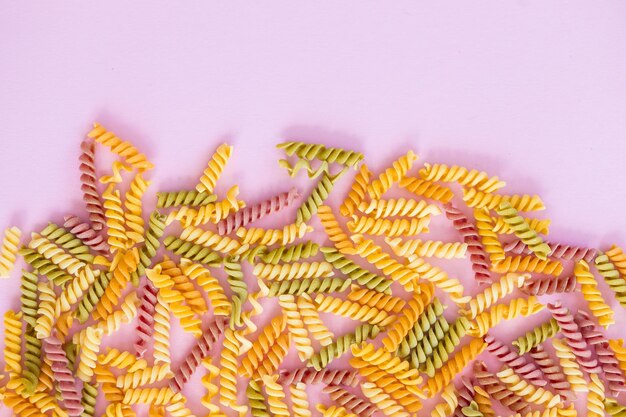 Beautiful Italian uncooked colored farfalle pasta closeup on pink background horizontal top view